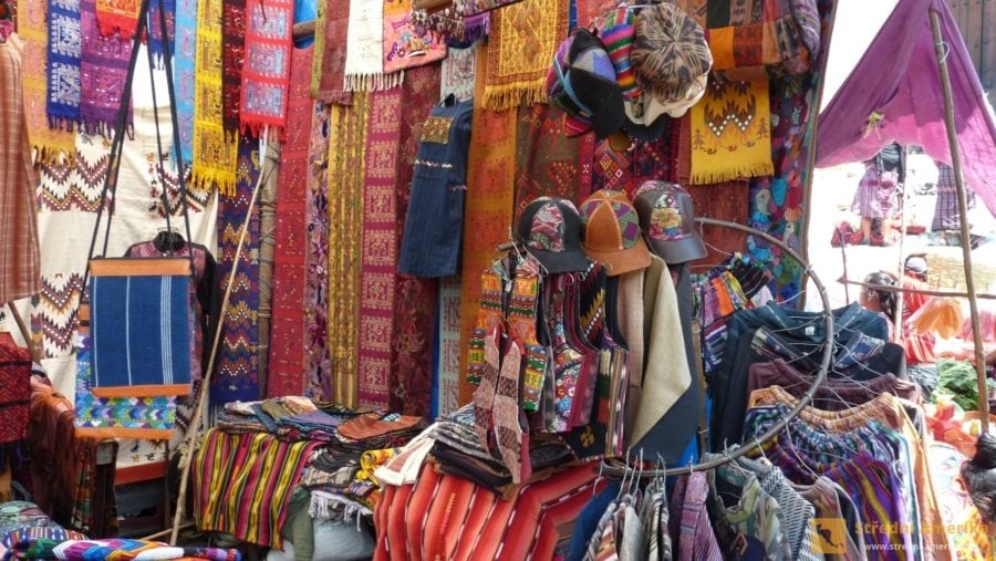 Guatemala, Chichicastenango. Drobnější textilie na trhu jsou levné, proto o mají velký zájem turisté.